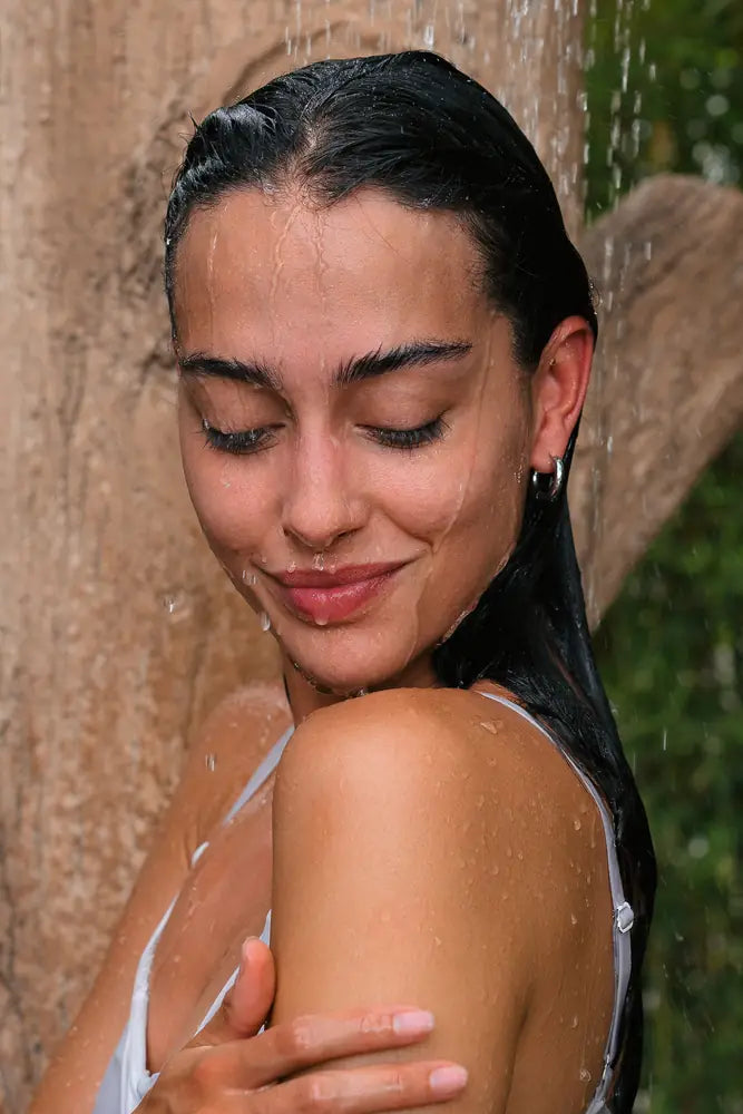 Mujer con el cabello mojado sonriendo debajo de la regadera.