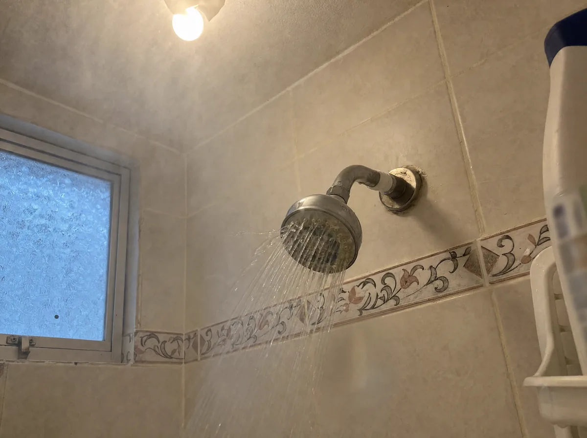 Regadera abierta con vapor y luz de mañana en un baño.
