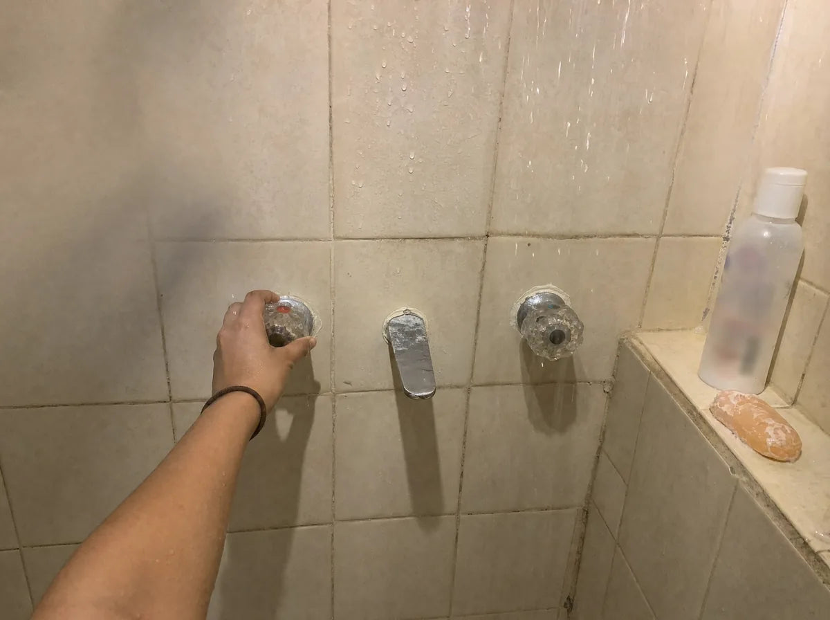 Mano abriendo la llave del agua caliente de la regadera.